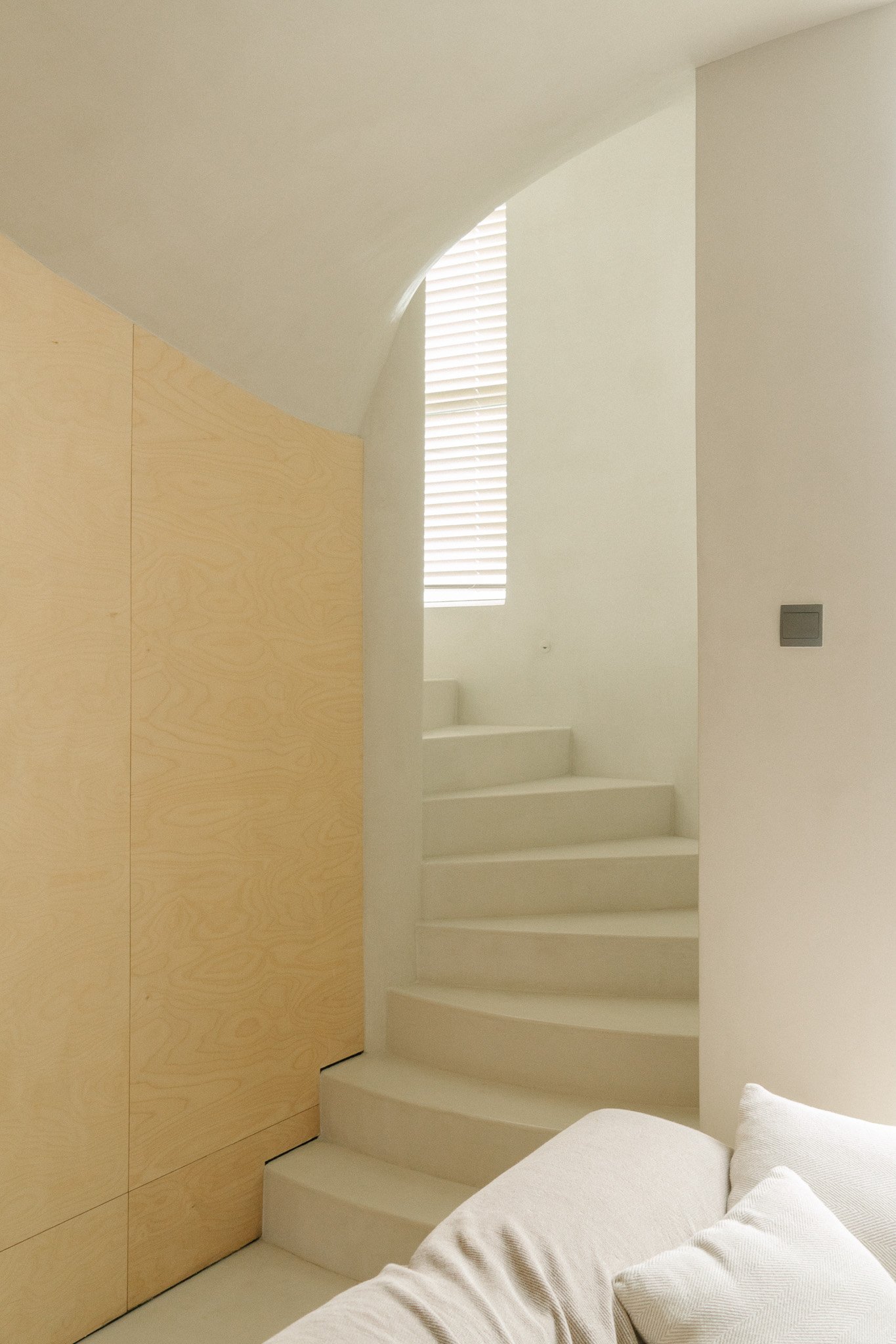 Curved birch plywood wardrobe beside a plastered spiral staircase in a Singapore home, Roger&Sons joinery